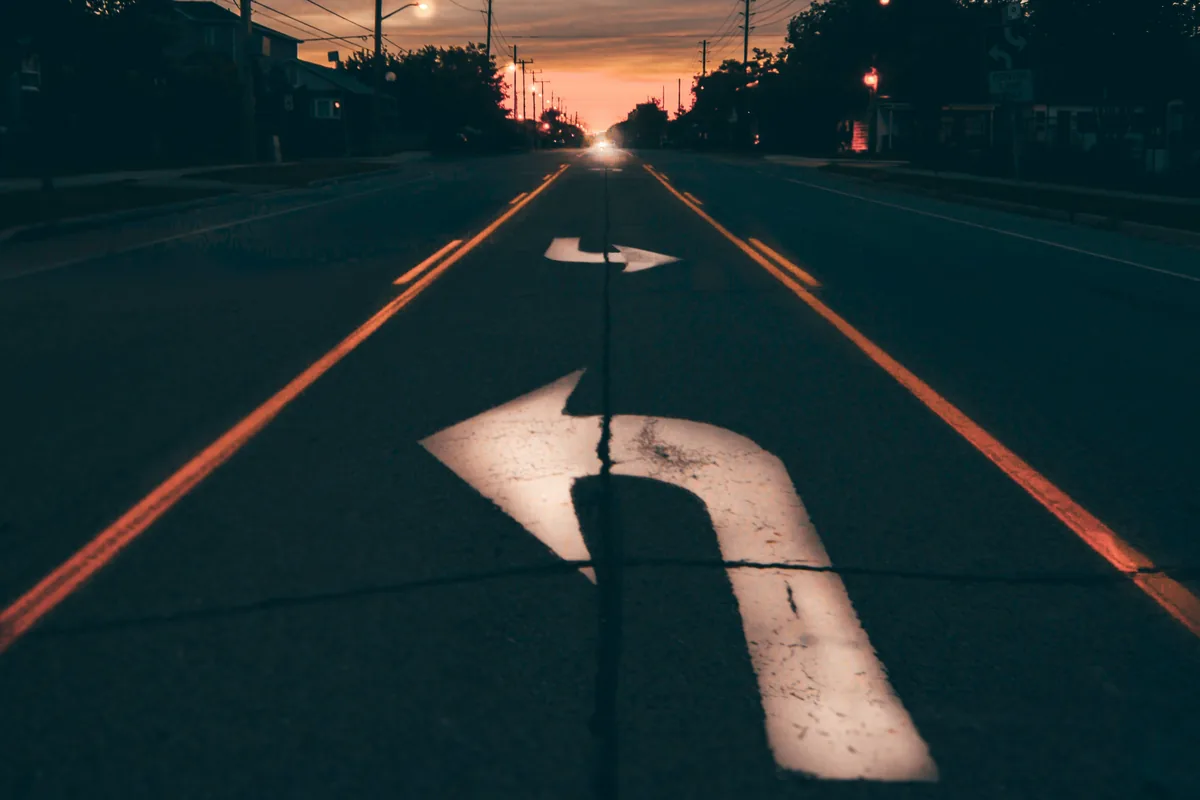 Carretera al atardecer con flechas pintadas en el asfalto señalando distintas direcciones, símbolo de la decisión entre invertir en fondos o ETF
