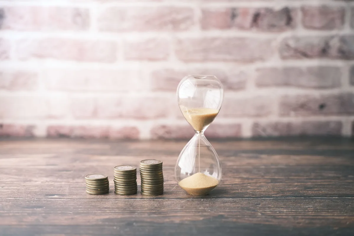Qué es invertir a largo plazo: reloj de arena junto a pilas crecientes de monedas