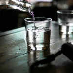 Agua vertiéndose de una botella a un vaso sobre una mesa de madera, metáfora del traspaso de dinero de un fondo a otro
