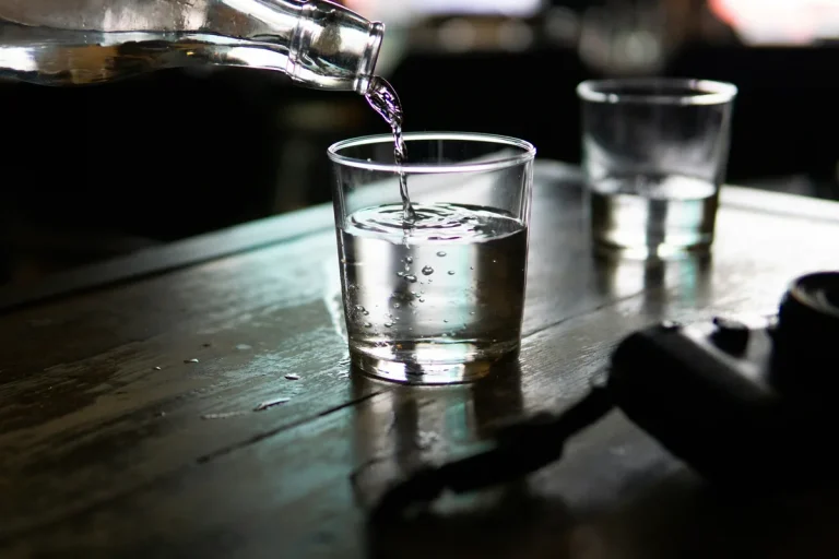 Agua vertiéndose de una botella a un vaso sobre una mesa de madera, metáfora del traspaso de dinero de un fondo a otro