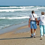 Pareja jubilada paseando de la mano por la orilla del mar, ilustrando el ahorro para la jubilación y los planes de pensiones