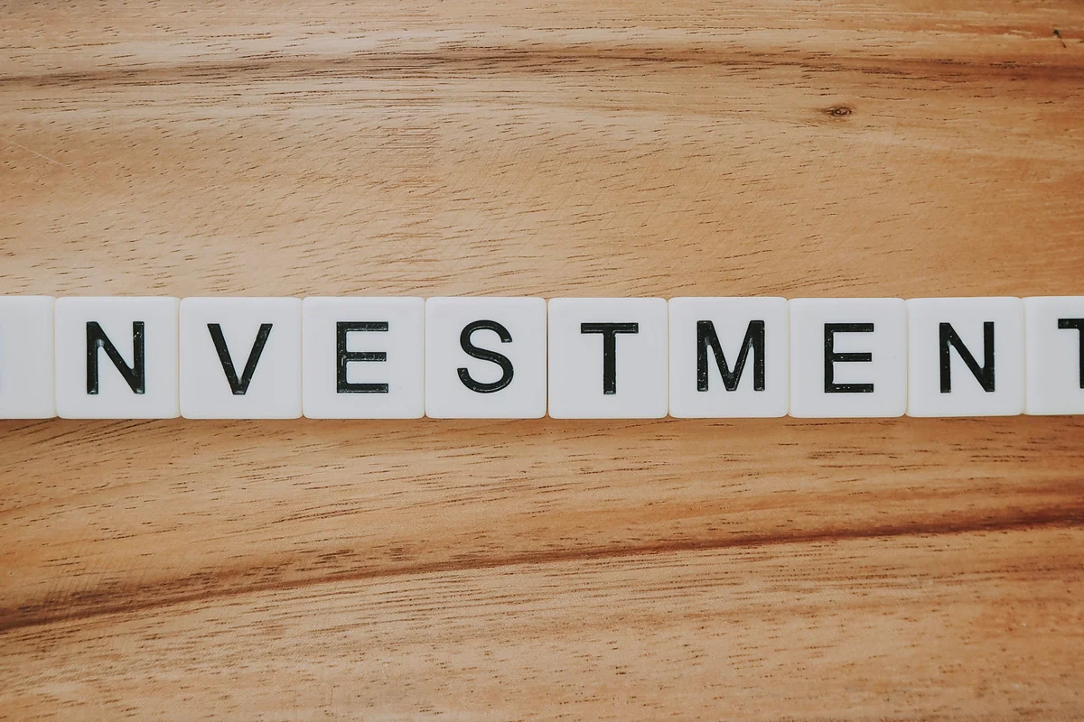 Bloques de madera con la palabra "INVESTMENT" sobre una superficie de madera, ilustrando el concepto de inversión a largo plazo en planes de pensiones.