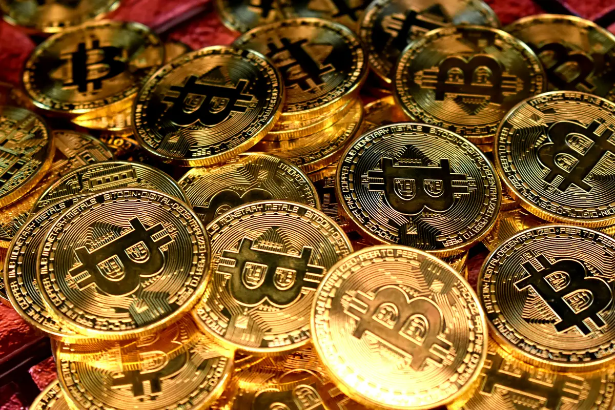 Montón de monedas físicas doradas con el símbolo de Bitcoin sobre fondo rojo, representando la criptomoneda.