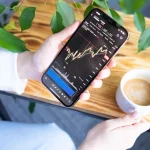 FOMO en la inversión: persona mirando el móvil con una app de bolsa subiendo (la eliges tú)