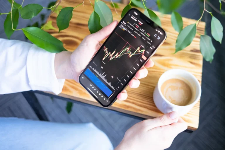 FOMO en la inversión: persona mirando el móvil con una app de bolsa subiendo (la eliges tú)