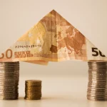 Billete de 50 euros doblado como tejado sobre dos columnas de monedas, concepto de fondos o ETF