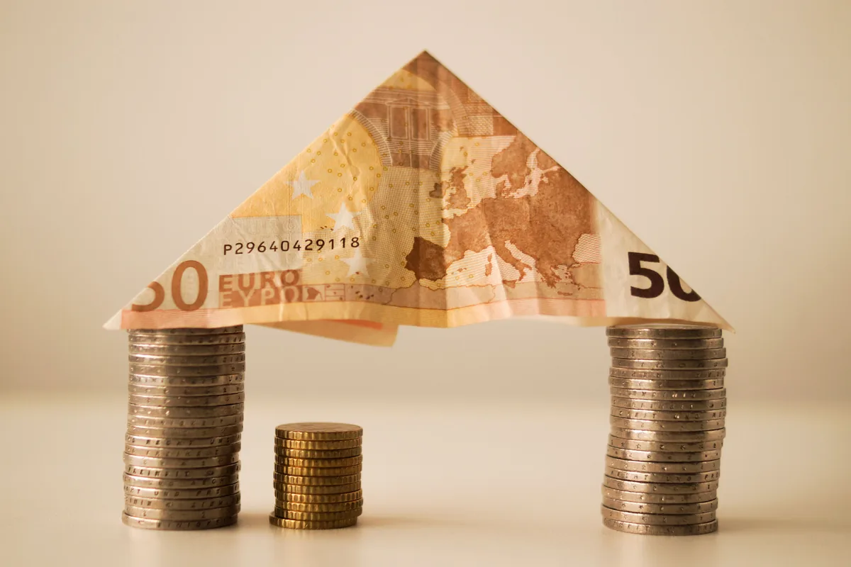 Billete de 50 euros doblado como tejado sobre dos columnas de monedas, concepto de fondos o ETF